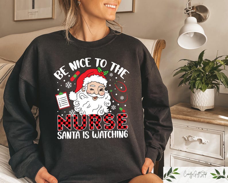 May include: Black sweatshirt with a red and white plaid design. The text "Be Nice To The Nurse Santa Is Watching" is printed on the front of the sweatshirt. A cartoon image of Santa Claus is above the text.