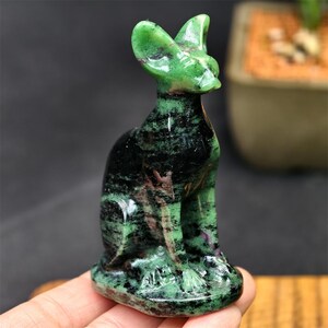 May include: A green and black stone cat figurine. The cat is sitting upright with its ears perked up. The stone has a marbled appearance with green and black colors. The figurine is a decorative item.