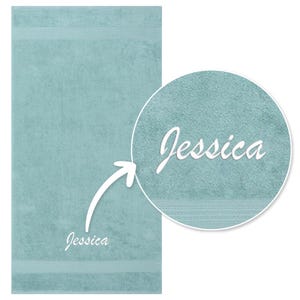 May include: A light blue bath towel with the name "Jessica" embroidered in white. The towel has a textured surface and a decorative stripe near the top and bottom.