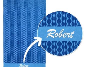 May include: A rectangular blue bath towel featuring a repeating geometric diamond pattern in darker blue shades. A horizontal light blue band near the bottom displays the name Robert in white script lettering, with a circular inset showing a close-up.
