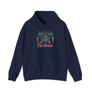 Può includere: Felpa con cappuccio blu navy con una tasca bianca e il testo "Just a girl who loves Christmas" in verde e rosa con una stringa di luci e due piccole figure su entrambi i lati del testo.
