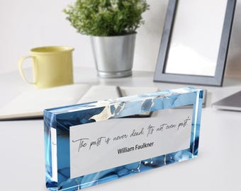 May include: A rectangular acrylic paperweight featuring a blue and white marbled pattern with gold accents. The center displays the text: The past is never dead. It's not even past. William Faulkner, printed in a black script and sans-serif font.