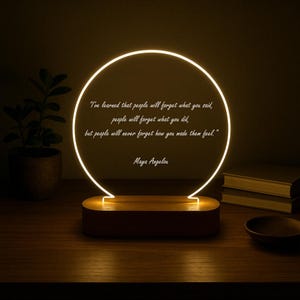 May include: A decorative lamp with a glowing circular design. The lamp features a wooden base and a bright, illuminated circle with the quote "I've learned that people will forget what you said..." by Maya Angelou.
