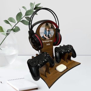 May include: A wooden stand with a photo of a young person playing video games. The stand has slots for two controllers and a headset. The text "Best console gamer of the year" is engraved on the stand.