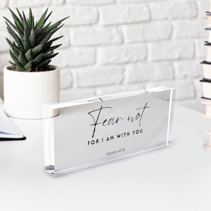 May include: A clear acrylic block with the words "Fear not, for I am with you" in black script. The text is from Isaiah 41:10. A small potted succulent and a stack of books are in the background.