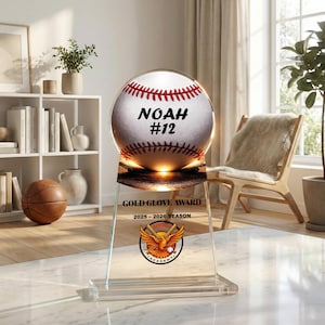 Op de afbeelding: Een honkbal Gold Glove Award trofee. De trofee heeft een honkbal met de naam "NOAH" en het nummer "#12" erop gedrukt. De basis van de trofee heeft de tekst "GOLD GLOVE AWARD" en "2025-2026 SEASON" met een adelaarslogo.