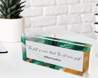 May include: A rectangular acrylic block with a green and gold marbled design. The block features a white rectangular insert with the quote "The past is never dead. It's not even past." by William Faulkner.