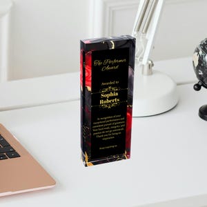 Puede incluir: Una placa de premio de vidrio negro y rojo con letras doradas. La placa dice "Top Performer Award" y "Awarded to Sophia Roberts". La placa tambi&eacute;n incluye un mensaje de reconocimiento por el desempe&ntilde;o excepcional y la b&uacute;squeda constante de la grandeza.