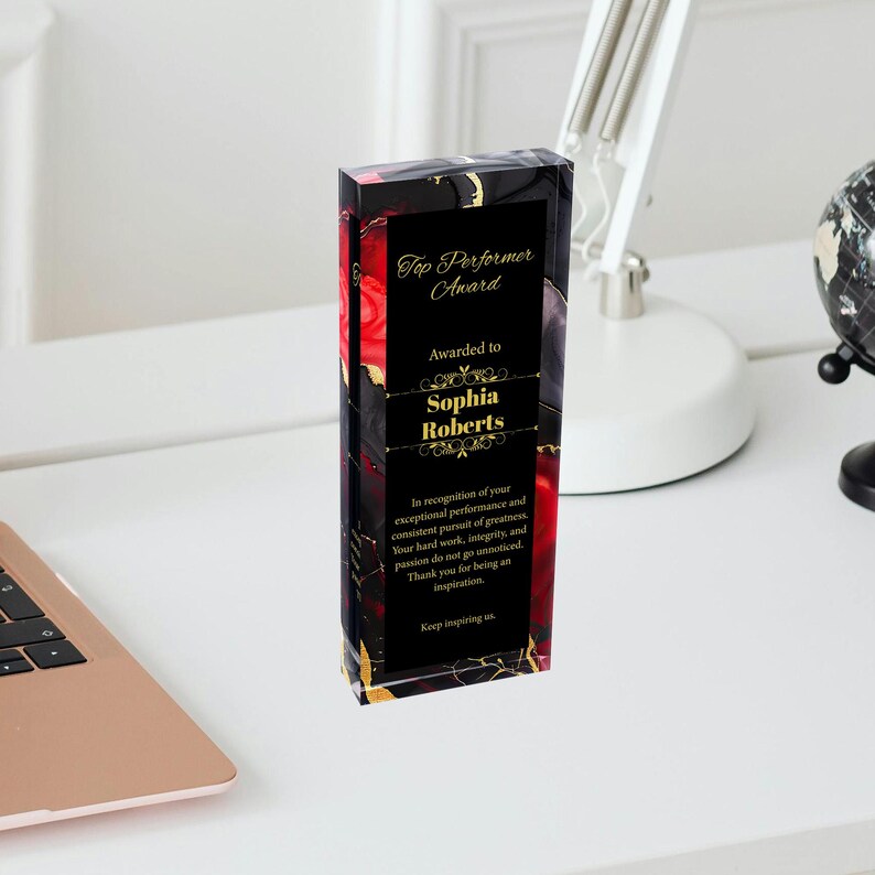 Puede incluir: Una placa de premio de vidrio negro y rojo con letras doradas. La placa dice "Top Performer Award" y "Awarded to Sophia Roberts". La placa tambi&eacute;n incluye un mensaje de reconocimiento por el desempe&ntilde;o excepcional y la b&uacute;squeda constante de la grandeza.