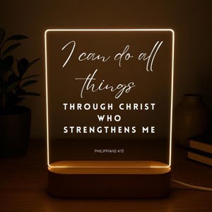 May include: A rectangular LED night light with a wooden base. The light displays the text "I can do all things through Christ who strengthens me" from Philippians 4:13 in white script. The light is on, illuminating the text.