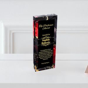 Puede incluir: Un premio acr&iacute;lico negro con letras doradas. El premio es para "Top Performer" y se otorga a "Sophia Roberts". El premio tiene un dise&ntilde;o abstracto rojo y negro.