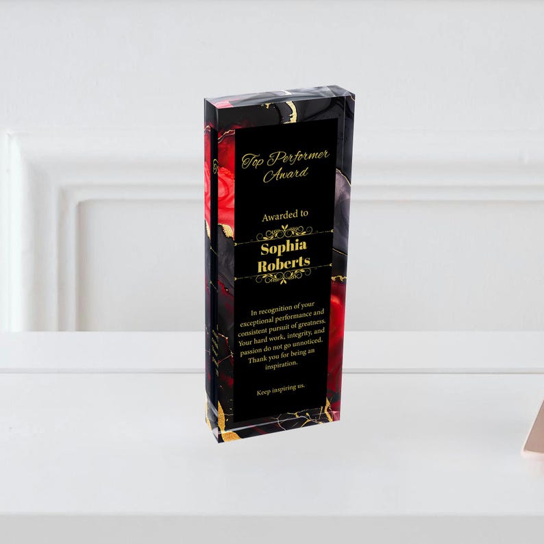 Puede incluir: Un premio acr&iacute;lico negro con letras doradas. El premio es para "Top Performer" y se otorga a "Sophia Roberts". El premio tiene un dise&ntilde;o abstracto rojo y negro.