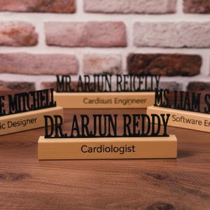 May include: A collection of personalised desk nameplates. Each nameplate has a black name and title on a light-coloured wooden base. The names include "Mr. Arjun Reicelly", "E. Mitchell", "Dr. Arjun Reddy", and "Ms. Liam S."