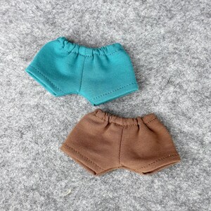 Puede incluir: Dos pares de pantalones cortos para mu&ntilde;ecas. Un par es de color verde azulado y el otro marr&oacute;n. Ambos pares tienen cintura el&aacute;stica y est&aacute;n hechos de una tela suave. Los pantalones cortos est&aacute;n dise&ntilde;ados para una mu&ntilde;eca o figura peque&ntilde;a.