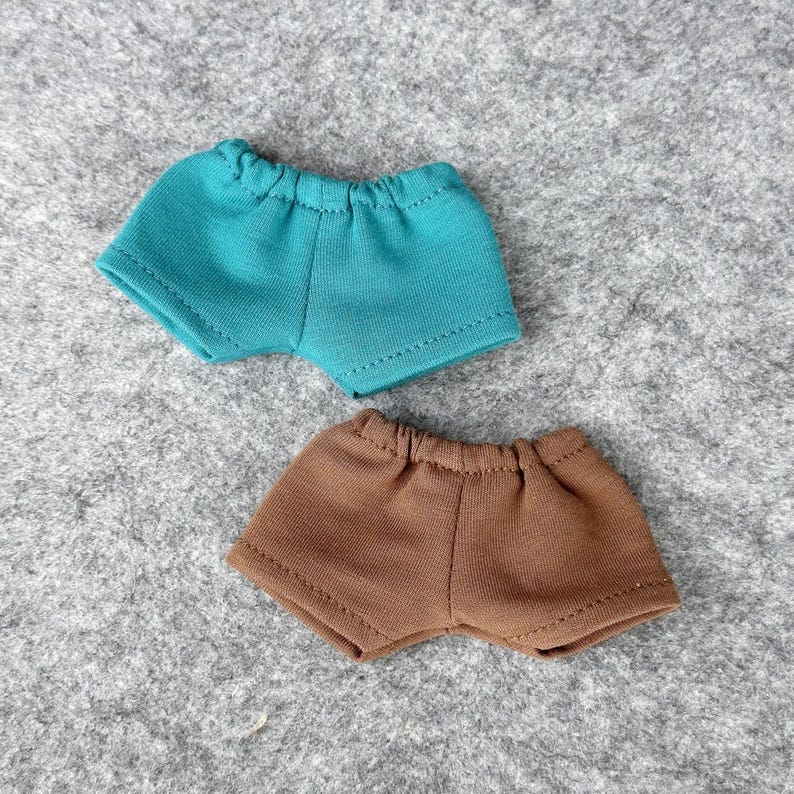 Puede incluir: Dos pares de pantalones cortos para mu&ntilde;ecas. Un par es de color verde azulado y el otro marr&oacute;n. Ambos pares tienen cintura el&aacute;stica y est&aacute;n hechos de una tela suave. Los pantalones cortos est&aacute;n dise&ntilde;ados para una mu&ntilde;eca o figura peque&ntilde;a.