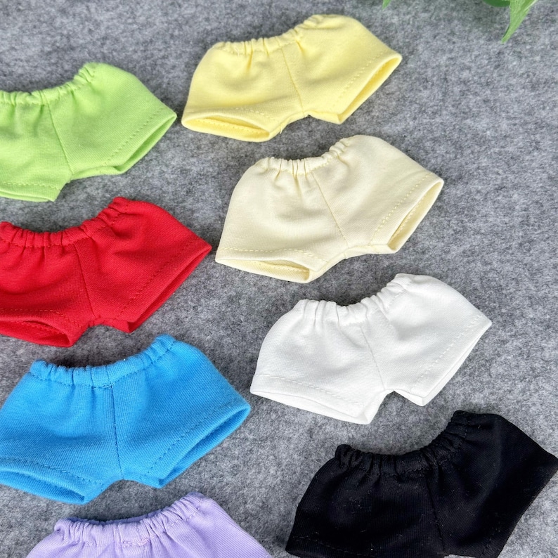 Puede incluir: Una colecci&oacute;n de pantalones cortos de mu&ntilde;eca de colores en varios tonos, incluyendo verde, amarillo, rojo, azul, blanco, negro y morado. Los pantalones cortos son de tela suave y tienen cintura el&aacute;stica.