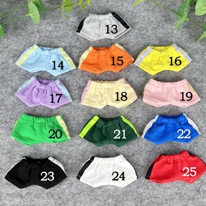 Puede incluir: Una colecci&oacute;n de shorts en miniatura en varios colores, incluyendo gris, azul, naranja, amarillo, morado, rosa, verde y blanco. Cada par tiene un ribete en contraste y un n&uacute;mero impreso. Los shorts est&aacute;n dispuestos sobre una superficie gris.