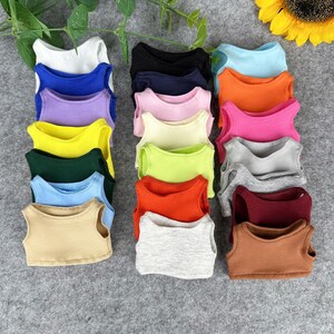 Peut inclure: Une collection de d&eacute;bardeurs pour poup&eacute;es aux couleurs vives, dont blanc, bleu, violet, jaune, vert, orange, rose, gris et marron. Les hauts sont dispos&eacute;s pour mettre en valeur leurs diff&eacute;rentes teintes et styles.