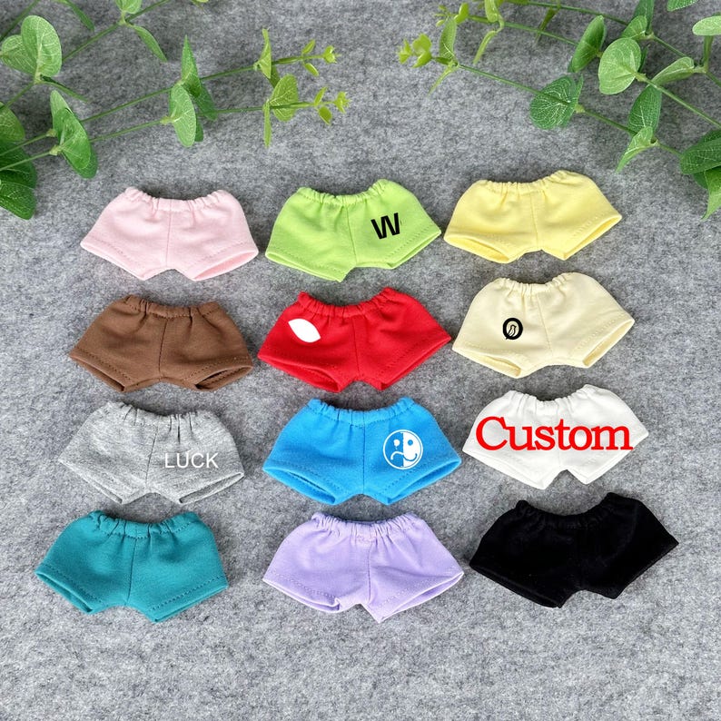 Puede incluir: Una colecci&oacute;n de pantalones cortos en miniatura en varios colores, incluyendo rosa, verde, amarillo, marr&oacute;n, rojo, crema, gris, azul, turquesa, morado y negro. Algunos pantalones cortos presentan texto o gr&aacute;ficos como "W", "LUCK", "Custom" y un s&iacute;mbolo de yin-yang.