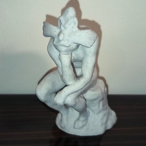 Könnte beinhalten: Eine weiße, 3D-gedruckte Skulptur einer Person, die mit dem Kopf in der Hand sitzt und der berühmten Statue "Der Denker" ähnelt.