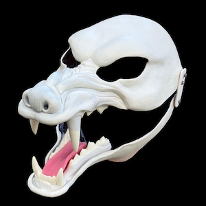 May include: A white furry mask with a large open mouth, showing sharp teeth and a pink tongue. The mask has a strap for attaching to the head.