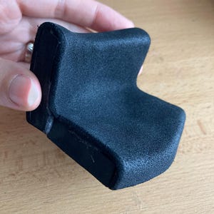 Könnte beinhalten: Ein schwarzes, weiches, gepolstertes U-förmiges Objekt mit einer glatten Oberfläche. Das Objekt besteht aus einem weichen, flexiblen Material und hat eine leicht abgerundete Form.