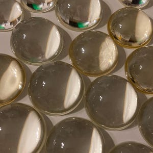 May include: A collection of clear glass decorative marbles, some with a slight iridescent sheen. The marbles are round and smooth, with a variety of sizes.