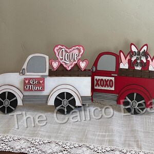 以下が含まれることがあります： 後ろに「Love」と書かれたハートが付いた白と赤のウッドトラック。トラックはハートと「Be Mine」と「XOXO」の文字で飾られています。トラックは「Loads of Love」と書かれたウサギの荷物を積んでいます。