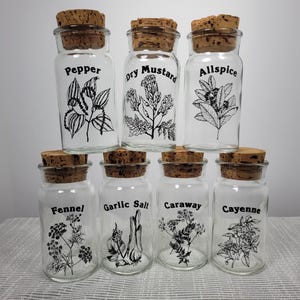 May include: Eight glass spice jars with cork lids and black labels. The labels have the names of spices: Pepper, Dry Mustard, Allspice, Fennel, Garlic Salt, Caraway, Cayenne.