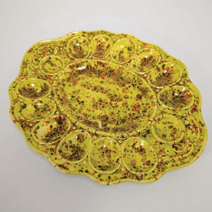 May include: A yellow ceramic deviled egg serving platter with a speckled design in red, brown, and black. The platter has a scalloped edge and individual egg-shaped compartments around the perimeter, with a central serving area.