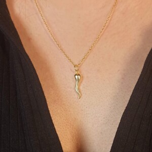 Könnte beinhalten: Eine goldfarbene Halskette mit einem kleinen, hornförmigen Anhänger. Der Anhänger hängt an einer zarten Kette. Die Halskette wird über einem schwarzen Oberteil getragen.