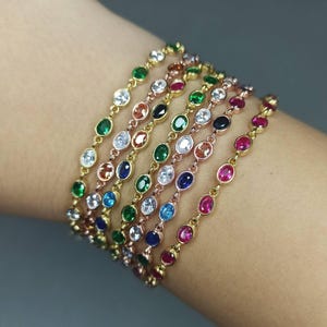 Pode incluir: Um conjunto de sete pulseiras com pedras preciosas de diferentes cores. Cada pulseira tem uma corrente com pedras preciosas de forma oval em uma variedade de cores, incluindo vermelho, azul, verde e transparente.