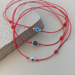 Può includere: Tre braccialetti di corda rossa con ciondoli di occhio turco di diversi colori. I ciondoli sono blu, azzurro e bianco.