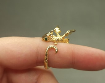 May include: A gold-colored dragon ring with green eyes. The dragon is curled around the finger and has its wings spread out.