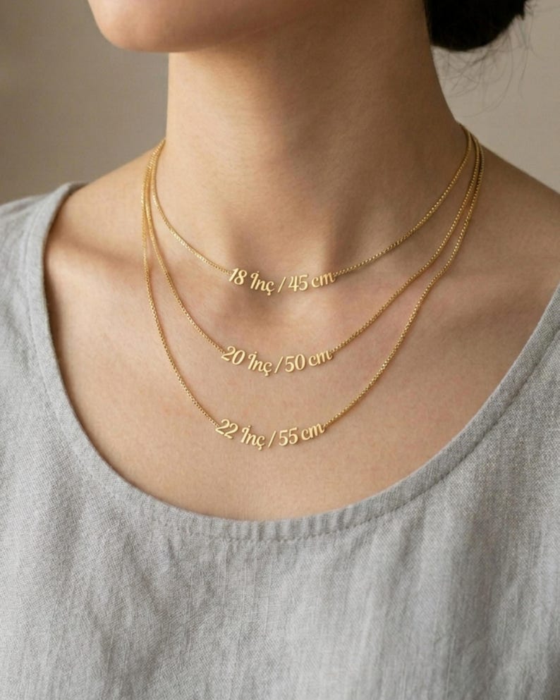 May include: Three delicate gold necklaces of varying lengths are displayed. The shortest necklace is 18 inches (45 cm), the middle one is 20 inches (50 cm), and the longest is 22 inches (55 cm). Each necklace has a small pendant with the length in inches and centimeters.