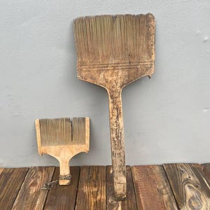 May include: Two wooden wool combs with long, thin, parallel metal teeth. The larger comb features a long handle and a wide head, while the smaller comb has a shorter handle with a piece of twine attached to the base. Both tools show signs of wear.