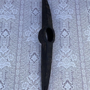Op de afbeelding: Een zwarte metalen pickaxe met een houten steel. De pickaxe heeft een scherpe punt en een platte kop.