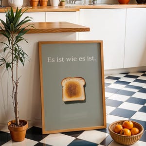 Könnte beinhalten: Ein gerahmter Druck mit grünem Hintergrund und dem Text "Es ist wie es ist." in Weiß. Ein Stück Toastbrot ist mittig auf dem Druck platziert.