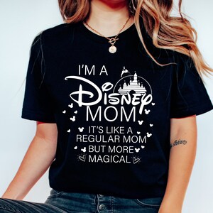 May include: Black t-shirt with white text that reads "I'M A Disney MOM" with a castle graphic. The shirt also says "IT'S LIKE A REGULAR MOM BUT MORE MAGICAL" with Mickey Mouse head accents.