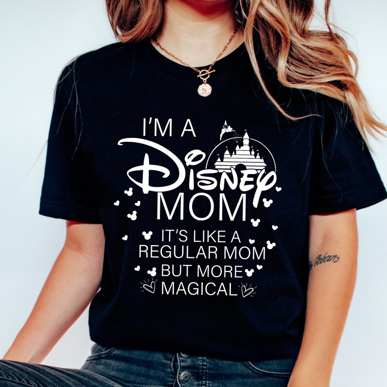 May include: Black t-shirt with white text that reads "I'M A Disney MOM" with a castle graphic. The shirt also says "IT'S LIKE A REGULAR MOM BUT MORE MAGICAL" with Mickey Mouse head accents.