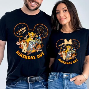 May include: Black t-shirts with a colorful graphic featuring characters from The Lion King. One shirt says "Daddy of the Birthday Boy" and the other says "Mom of the Birthday Boy". The design includes Simba, Timon, Pumbaa, and other characters.