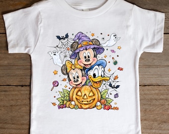 May include: White toddler t-shirt featuring Mickey Mouse, Minnie Mouse, and Donald Duck in Halloween costumes. The design includes a jack-o'-lantern, ghosts, candy, and spiderwebs. The characters are wearing a witch hat and bow.