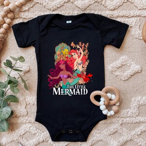 Puede incluir: Mono negro para beb&eacute; con un estampado gr&aacute;fico de Ariel, &Uacute;rsula y Flounder de La Sirenita. El texto "The Little Mermaid" est&aacute; impreso debajo de los personajes.