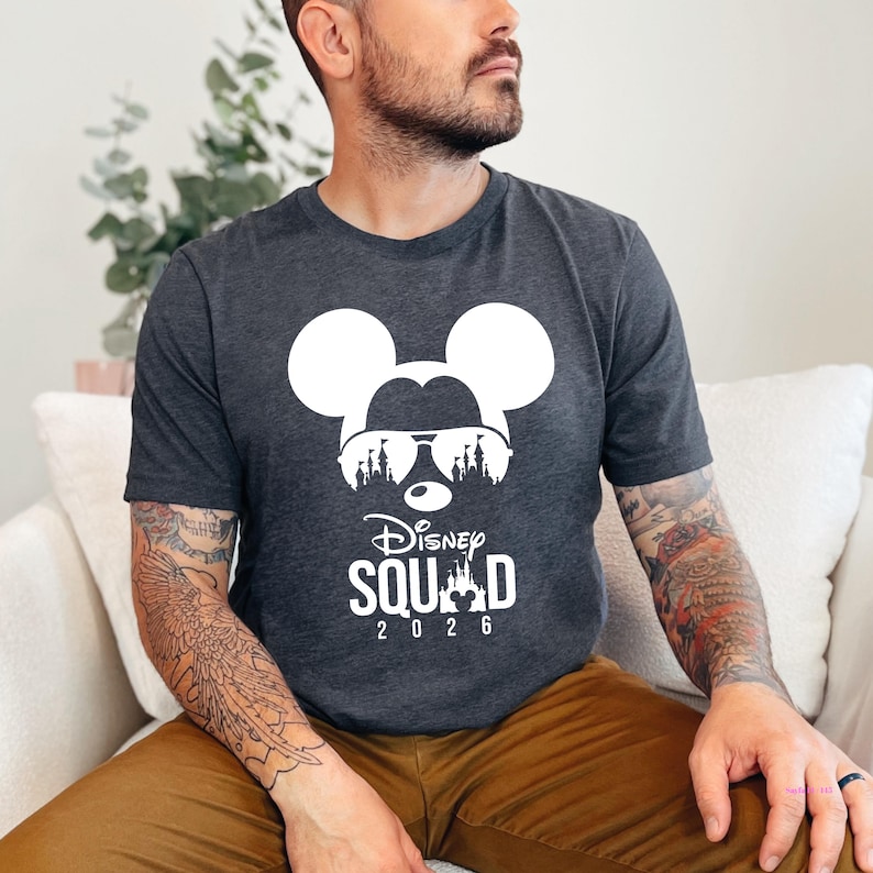 May include: Dark gray t-shirt featuring a white Mickey Mouse silhouette wearing sunglasses with a castle design. The text "Disney Squad 2026" is printed below the graphic. The shirt is made of a soft material.