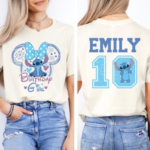 May include: Cream-colored t-shirt featuring a blue cartoon character design. The front of the shirt has the text "Birthday Girl" and the character's image. The back displays the name "Emily" and the number "10" with the character's image.