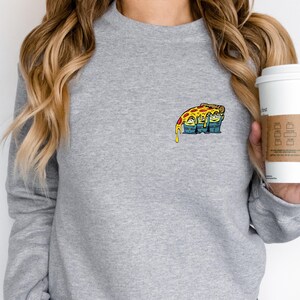 May include: A gray sweatshirt featuring a colorful cartoon pizza slice graphic on the chest. The pizza has melted cheese and is resting on top of three green aliens. The sweatshirt has long sleeves and a crew neck.