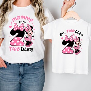 K&ouml;nnte beinhalten: Wei&szlig;e T-Shirts mit Minnie-Maus-Motiv. Ein Shirt hat den Text "Mommy of the 2 Toodles" mit einer Minnie-Maus-Grafik und rosa Punkten. Das andere Shirt hat den Text "Oh, 2 Toodles" mit einem &auml;hnlichen Design.