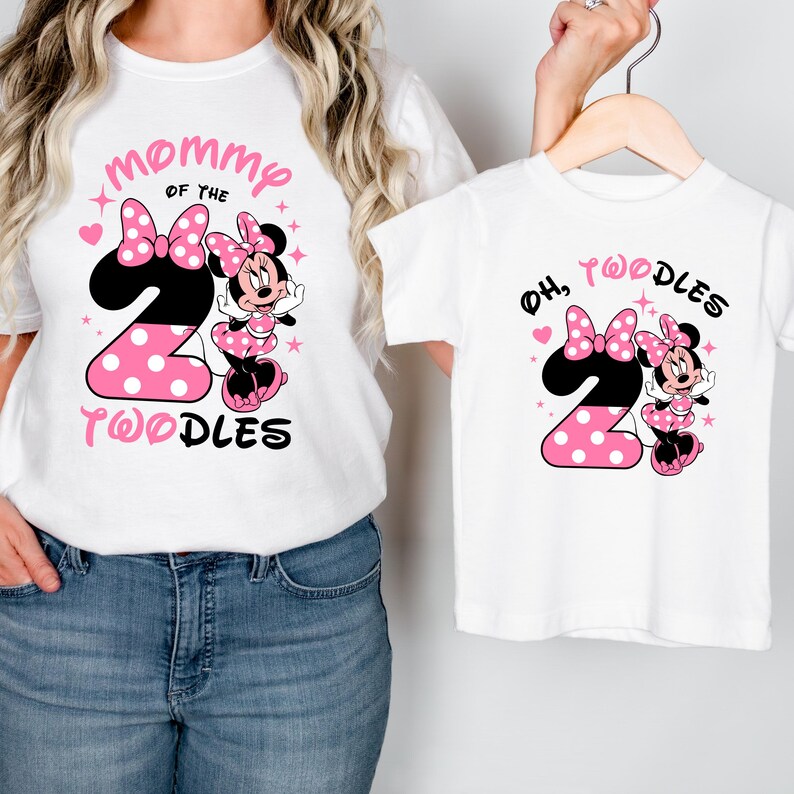 K&ouml;nnte beinhalten: Wei&szlig;e T-Shirts mit Minnie-Maus-Motiv. Ein Shirt hat den Text "Mommy of the 2 Toodles" mit einer Minnie-Maus-Grafik und rosa Punkten. Das andere Shirt hat den Text "Oh, 2 Toodles" mit einem &auml;hnlichen Design.