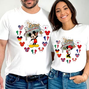 May include: White t-shirts featuring Mickey and Minnie Mouse with the Epcot logo. Mickey is in a red and yellow outfit, and Minnie wears a red bow. The design includes flags of various countries and Mickey Mouse silhouettes.