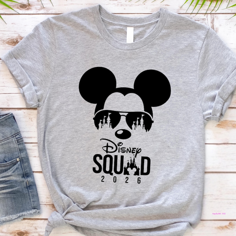 May include: A light gray t-shirt featuring a black graphic of Mickey Mouse wearing sunglasses with a silhouette of Disney characters. The text "Disney Squad 2026" is below the graphic.